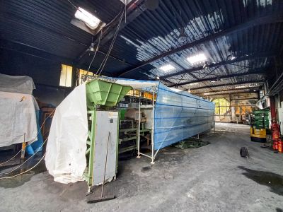 Industriehalle mit gr&uuml;ner Maschine, wei&szlig;er Plane und langem, blau verh&uuml;lltem Ger&uuml;staufbau.