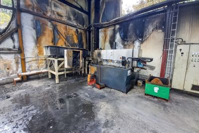 Brandschaden in einer Industriehalle mit ru&szlig;geschw&auml;rzten W&auml;nden, besch&auml;digten Maschinen und verkohlten Materialien.