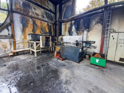 Brandschaden in einer Industriehalle mit ru&szlig;geschw&auml;rzten W&auml;nden, besch&auml;digten Maschinen und verkohlten Materialien.