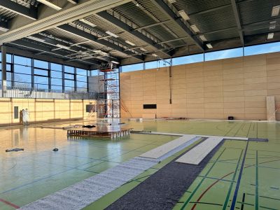 Sporthalle im Bauzustand mit gr&uuml;nem Boden, Spielfeldlinien, Ger&uuml;st und Schutzfolien w&auml;hrend der Renovierungsarbeiten.