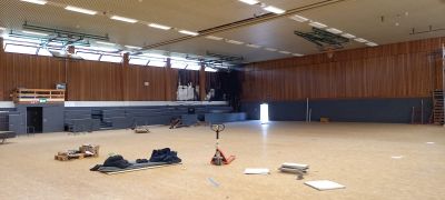 Leere Halle mit Holzverkleidung, ausgefahrenen Trib&uuml;nenelementen und Materialien auf dem Boden w&auml;hrend Umbauarbeiten.