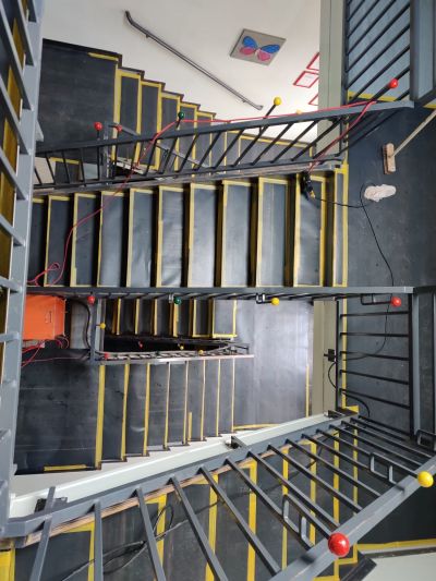 Blick von oben auf ein mehrst&ouml;ckiges Treppenhaus mit schwarz-gelben Stufen und Metallgel&auml;nder.