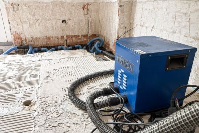 Blaues Bautrockner-Ger&auml;t der Marke Fixtron steht auf einem Estrichboden in einem Raum mit freigelegten W&auml;nden w&auml;hrend einer Bautrocknung.