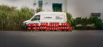 Wei&szlig;er PSM-Transporter parkt vor Gr&uuml;npflanzen, davor stehen Paletten mit roten Kanistern und Ger&auml;ten.