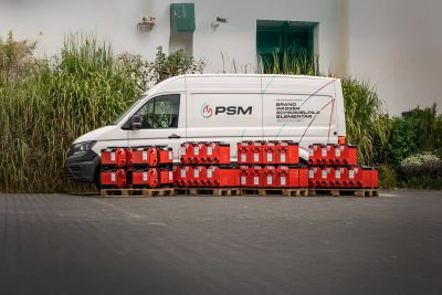 Wei&szlig;er PSM-Transporter parkt vor Gr&uuml;npflanzen, davor stehen Paletten mit roten Kanistern und Ger&auml;ten.