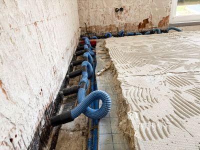 Blaue Trocknungsschl&auml;uche entlang der Wand verlegt, daneben frisch aufgetragener Fliesenkleber auf dem Boden.