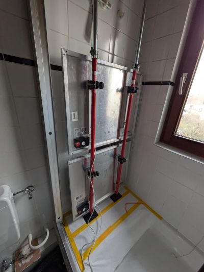Bautrocknungsger&auml;t mit Metallverkleidung und roten Rohrleitungen in einem gefliesten Badezimmer, auf Folie zum Schutz des Bodens.