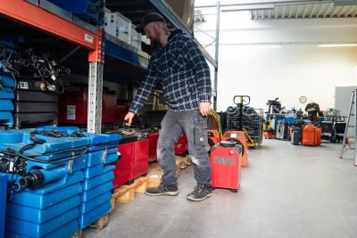 Mann in Warenlager sortiert blaue und rote Trocknungsger&auml;te f&uuml;r die Bautrocknung.