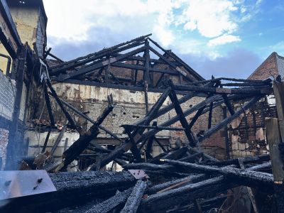 Ausgebranntes Geb&auml;ude mit eingest&uuml;rztem Dachstuhl und verkohlten Holzbalken vor bew&ouml;lktem Himmel.