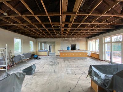 Renovierungsarbeiten in einem Raum mit offener Dachkonstruktion, Baustaub und Schutzabdeckungen nach Brandschaden.