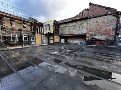 Brandgesch&auml;digtes Geb&auml;ude mit teilweise abgetragener Fassade, Ger&uuml;st und wassergef&uuml;llter Bodenplatte im Vordergrund.