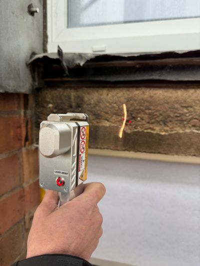 Handgehaltenes Messger&auml;t mit Laserpointer zur Untersuchung eines verkohlten Fensterrahmens auf Brandsch&auml;den.