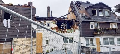 Brandgesch&auml;digtes Wohnhaus mit eingest&uuml;rztem Dach und verkohltem Dachstuhl, im Vordergrund ein Bauzaun.
