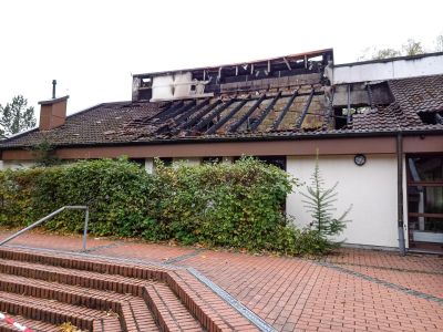 Besch&auml;digtes Hausdach mit verbrannten Dachbalken nach Brand, davor Hecke, Treppe und gepflasterter Weg.