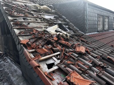 Stark besch&auml;digtes Dach mit herausgebrochenen Ziegeln, freiliegender D&auml;mmung und zerst&ouml;rter Dachkonstruktion nach Unwetter.