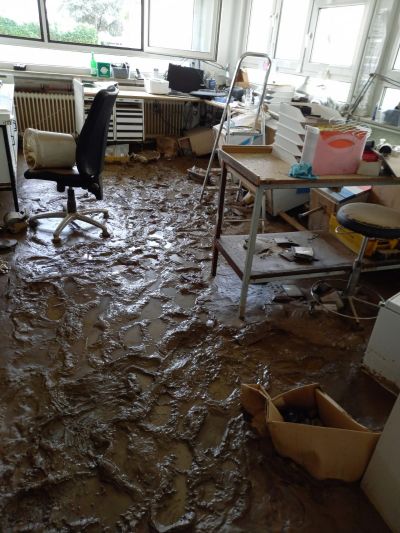 B&uuml;ro nach &Uuml;berschwemmung mit dickem Schlamm auf dem Boden, umgest&uuml;rztem B&uuml;rostuhl und verschmutzten M&ouml;beln.
