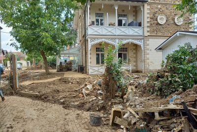 Historisches Geb&auml;ude mit Balkon, davor mit Schlamm und Tr&uuml;mmern &uuml;bers&auml;tes Grundst&uuml;ck nach Hochwasser.