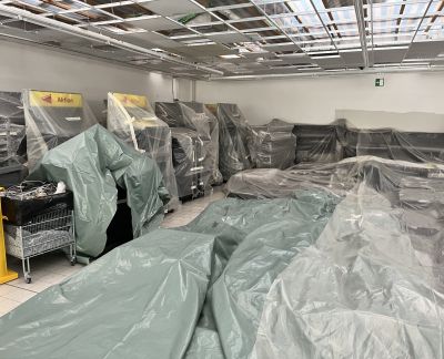 Ladenregale und Einrichtung, mit Schutzplanen abgedeckt, w&auml;hrend einer Renovierung mit offener Deckenkonstruktion.