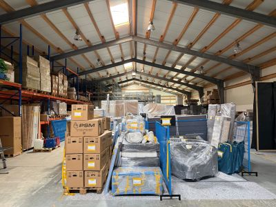 Lagerhalle mit gestapelten Kartons, verpackten M&ouml;beln und Waren auf Paletten unter einem Dach mit Metalltr&auml;gern.