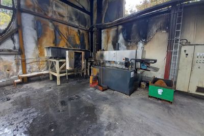 Fire-damaged industrial hall mit verru&szlig;ten W&auml;nden, besch&auml;digten Maschinen und einer Werkbank auf R&auml;dern.