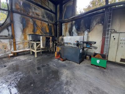 Fire-damaged industrial hall mit verru&szlig;ten W&auml;nden, besch&auml;digten Maschinen und einer Werkbank auf R&auml;dern.