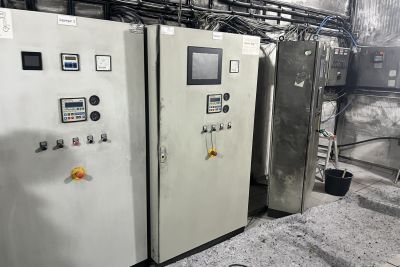 Zwei industrielle Schaltschr&auml;nke mit Displays und Bedienelementen in einer Werkstatt, daneben ein Edelstahlschrank und Kabel.