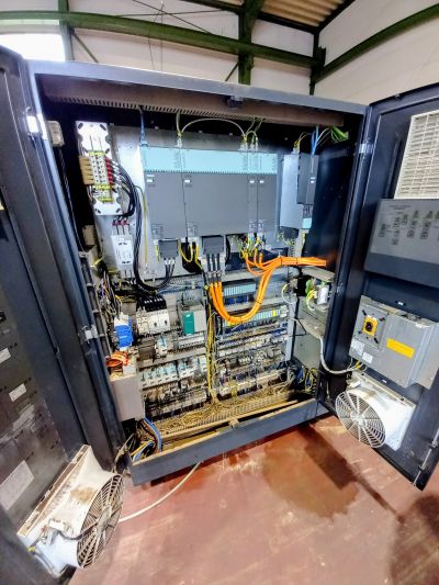 Offener Schaltschrank mit komplexer Verkabelung, Relais und elektronischen Komponenten in einer Industriehalle.