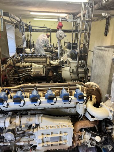 Industrieller Motor mit blauen Einspritzventilen wird in einem Maschinenraum von einer Person im Schutzanzug gewartet.