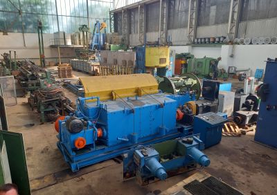 Gro&szlig;e blaue Industriemaschine in einer Werkshalle, umgeben von weiteren Maschinen und Anlagenteilen.