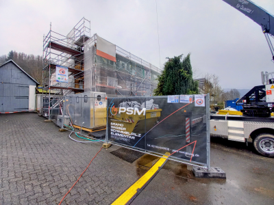 Bauger&uuml;st an einem Geb&auml;ude w&auml;hrend einer Schadstoffsanierung, mit PSM-Bauzaun-Werbebanner im Vordergrund.