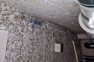 Deckenecke mit starkem Schimmelbefall und wei&szlig;en Ausbl&uuml;hungen, daneben eine L&uuml;ftungsleitung und Kabelverbindungen an der Wand.