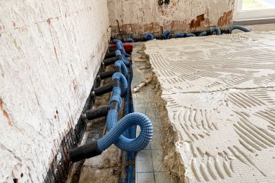 Blaue Wellrohre mit schwarzen Endkappen an Wand, daneben mit Kammspachtel vorbereiteter Estrich f&uuml;r Fliesenarbeiten.