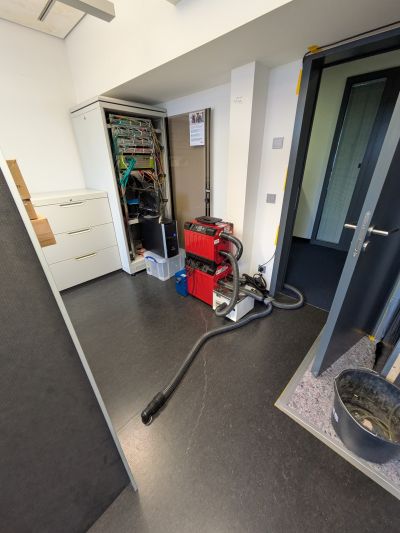 Trocknungsger&auml;te und Schl&auml;uche stehen in einem Raum mit offenem Serverschrank zur Trocknung nach einem Wasserschaden.