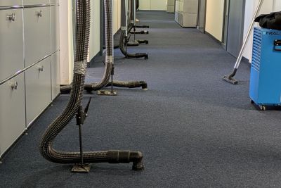 B&uuml;rokorridor mit Trocknungsschl&auml;uchen und Ventilatoren auf dem Teppichboden zur Wasserschadensanierung.