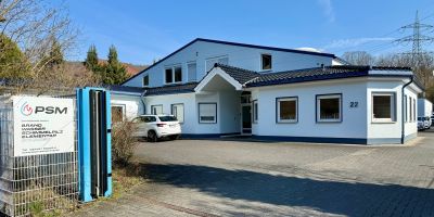 Wei&szlig;es Firmengeb&auml;ude von PSM in Brachbach, davor Parkplatz und Einfahrtstor.