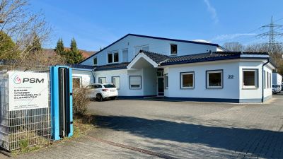 Wei&szlig;es Firmengeb&auml;ude von PSM in Brachbach, davor Parkplatz und Einfahrtstor.