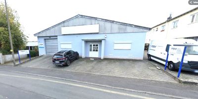 Blaues PSM Gewerbegeb&auml;ude in Friedrichsdorf mit Rolltor und Eingangst&uuml;r, davor geparktes Auto und wei&szlig;er Lieferwagen mit PSM-Beschriftung.