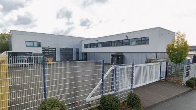 Modernes Firmengeb&auml;ude von PSM GmbH in Siegen mit grauer Fassade, Einfahrtstor und Metallzaun im Vordergrund.
