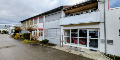 Zweist&ouml;ckiges PSM Geb&auml;ude in Ulm mit wei&szlig;er Fassade, roten Fensterrahmen und &uuml;berdachtem Balkon &uuml;ber dem Eingangsbereich.