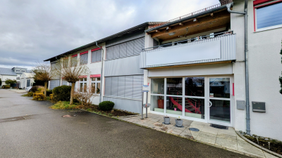 Zweist&ouml;ckiges PSM Geb&auml;ude in Ulm mit wei&szlig;er Fassade, roten Fensterrahmen und &uuml;berdachtem Balkon &uuml;ber dem Eingangsbereich.