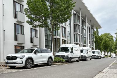 Wei&szlig;e PSM Fahrzeuge, darunter ein SUV und mehrere Transporter, parken vor einem modernen Wohngeb&auml;ude.