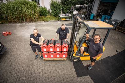 Drei Mitarbeiter von PSM GmbH stehen bei einem Gabelstapler mit einer Palette roter Kisten auf dem Firmenhof.